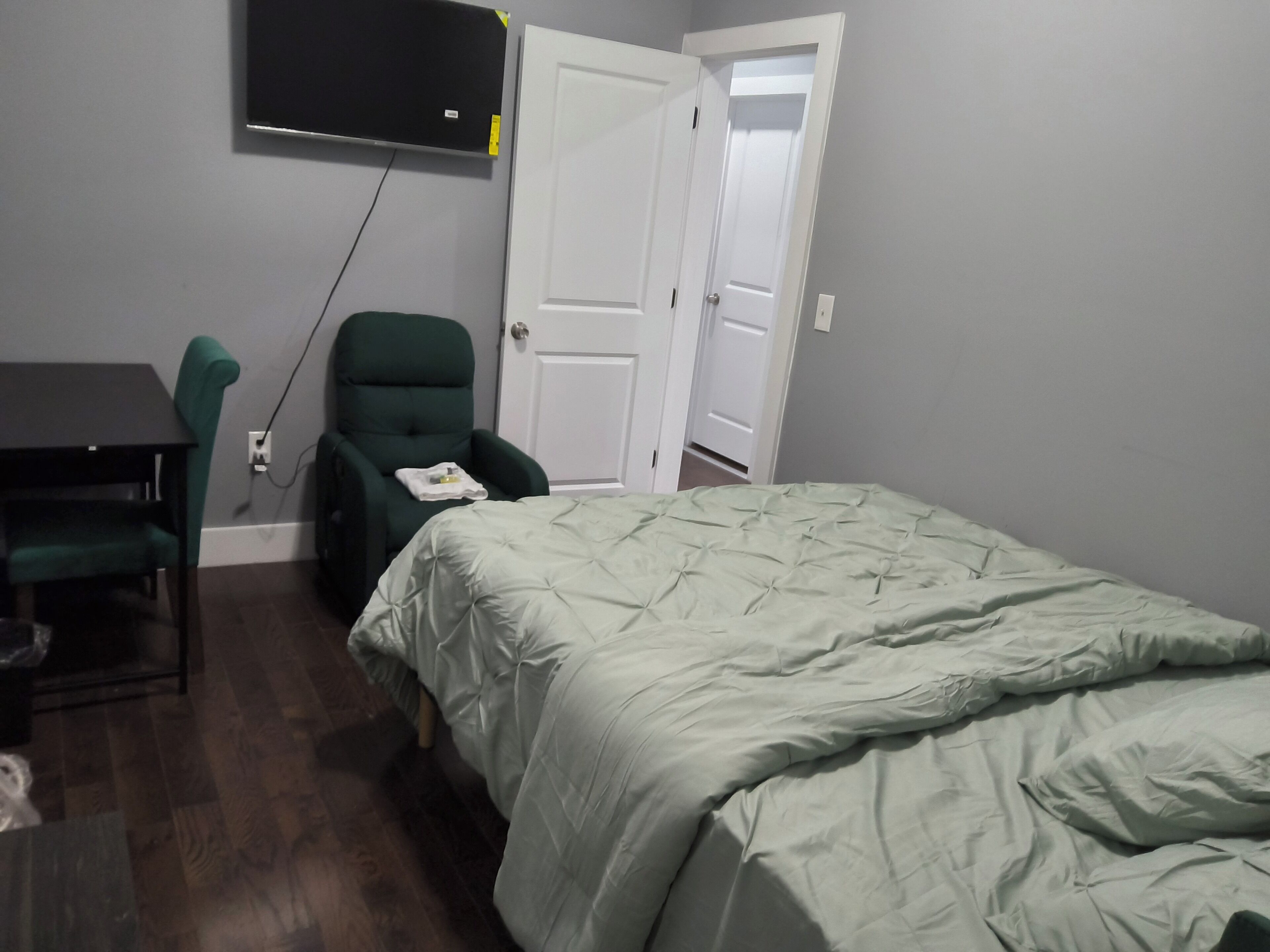 A room with a bed, a desk, a chair, and a TV mounted on the wall.