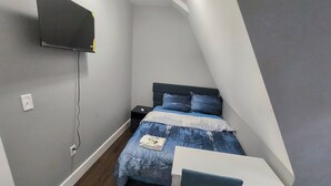 A small, modern bedroom with a bed, bedside table, and a desk with a chair.