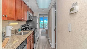 A compact kitchen with wooden cabinets, stainless steel appliances, and a view to a balcony.