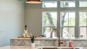 Una cocina con encimera de mármol, grifo dorado y ventana con vistas a árboles.