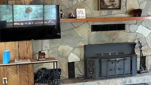 A stone fireplace with a television above it, a small table with a blue bag, and a shelf with decorative items.