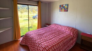 A bedroom with a large bed, a window with curtains, a small bedside table, and a ceiling light fixture. - cabañas nuevo amanecer paillaco valdivia (Paillaco)