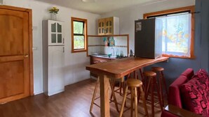 A compact kitchen with wooden flooring, a dining table with stools, a refrigerator, and cabinets. - cabañas nuevo amanecer paillaco valdivia (Paillaco)
