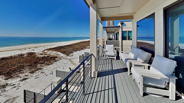Un balcon avec des chaises blanches et une vue sur la plage et l’océan.