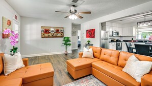 A modern living room with a sectional sofa, a ceiling fan, and artwork on the walls. - Breezy Lutz Home w/ Patio: Perfect for Long Stays (Lutz)