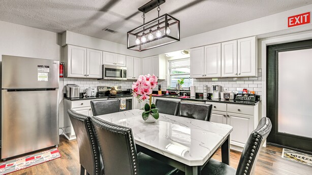 A modern kitchen with white cabinets, a stainless steel refrigerator, a dining table with chairs, and a hanging light fixture. - Breezy Lutz Home w/ Patio: Perfect for Long Stays (Lutz)
