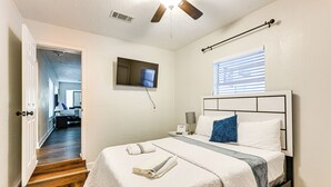 A bedroom with a bed, a TV mounted on the wall, a window with blinds, and a door leading to another room. - Breezy Lutz Home w/ Patio: Perfect for Long Stays (Lutz)