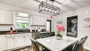 A modern kitchen with white cabinets, a marble countertop, and a dining area with a white table and black chairs. - Breezy Lutz Home w/ Patio: Perfect for Long Stays (Lutz)