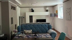 A modern living room with a blue sofa, a dining table with a floral table runner, and a white entertainment unit above the sofa. - Leiningerland, the gateway to the Palatinate Enjoy with all your senses/ Pets welcome (Obersülzen)