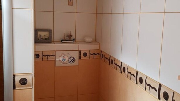 A bathroom with white tiles, a towel rack, a soap dispenser, and a small shelf with a framed picture. - Leiningerland, the gateway to the Palatinate Enjoy with all your senses/ Pets welcome (Obersülzen)