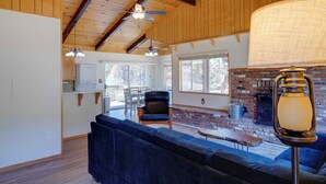 A spacious living room with a large blue sofa, a wooden ceiling, and a brick fireplace. - Mountain-View Haven w/ Deck in Pine Mountain Club (Frazier Park)