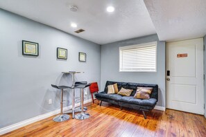 Quarto com sofá cinza escuro, dois banquetes, janela com persianas e porta com sinal de Wi-Fi.