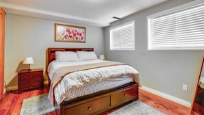 A bedroom with a wooden bed, a nightstand, a framed picture on the wall, and a window with blinds. - 12 Mi to Temple Square: Cozy + Convenient Apt! (Taylorsville)