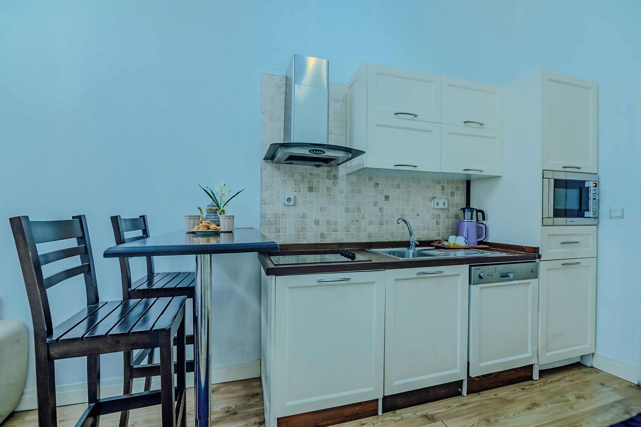 A compact kitchen with white cabinets, a built-in microwave, and a small dining area with a wooden table and chairs.