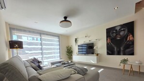 Un salon moderne avec un canapé gris, un téléviseur à écran plat et un grand tableau abstrait.