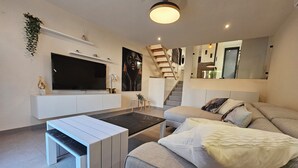 Un salon moderne doté d’un téléviseur à écran plat, d’un canapé, d’une table basse et d’un escalier menant à un niveau supérieur.
