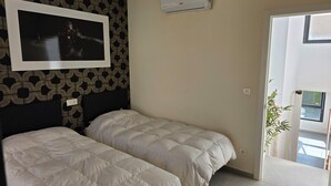 Une chambre d’hôtel avec deux lits, un téléviseur fixé au mur, un appareil de climatisation et une porte donnant sur un balcon.
