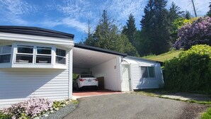 Une maison de plain-pied avec un garage, entourée d’une végétation luxuriante et d’arbres.