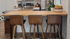Une cuisine moderne avec des meubles blancs, des appareils en acier inoxydable, un îlot central en bois doté de tabourets, et une orchidée en pot.