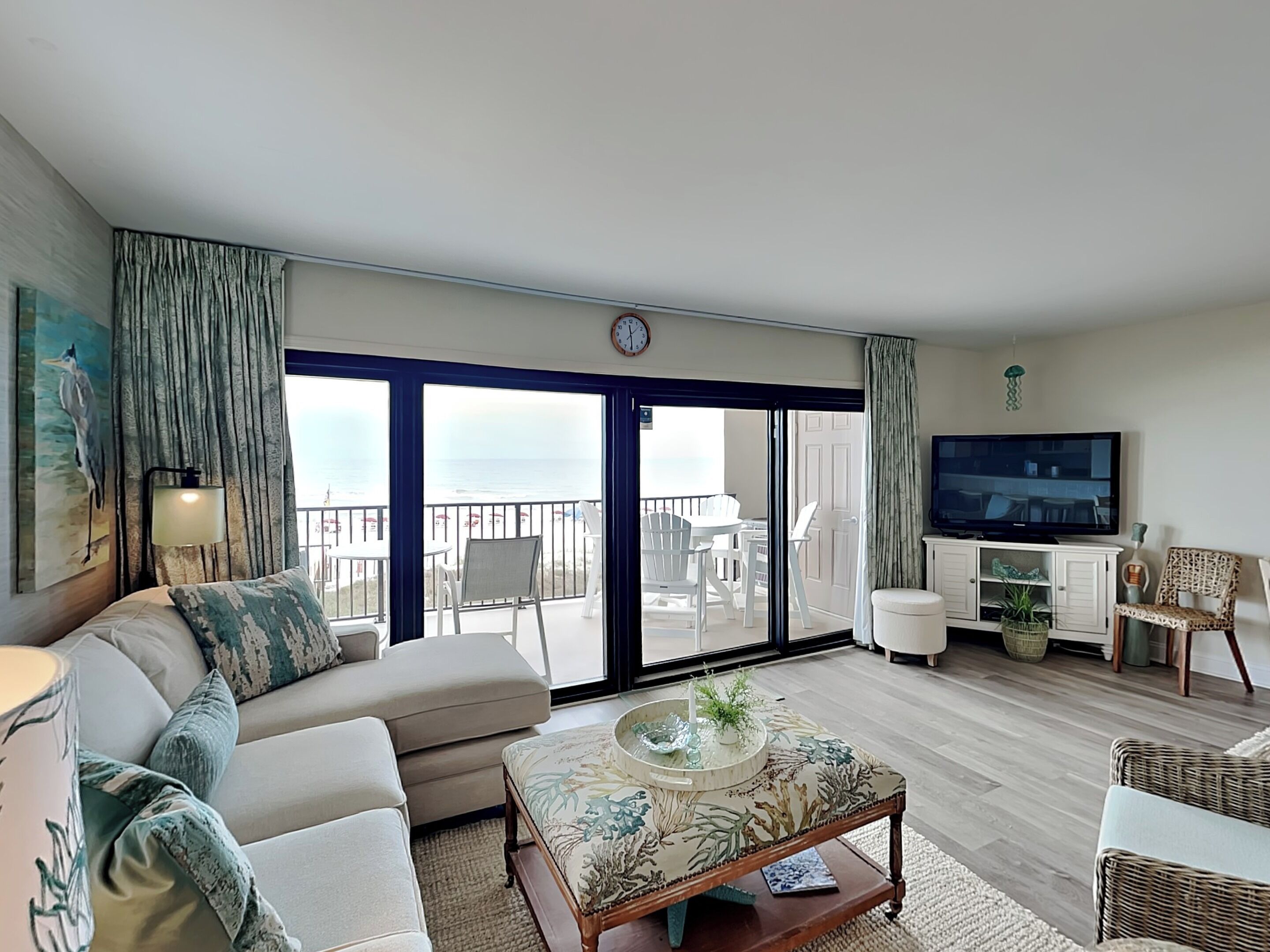 A living room with a sofa, a coffee table, a TV, and a balcony with a view of the sea.