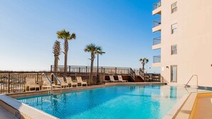 Une piscine avec des chaises longues, des palmiers et un bâtiment doté de balcons.