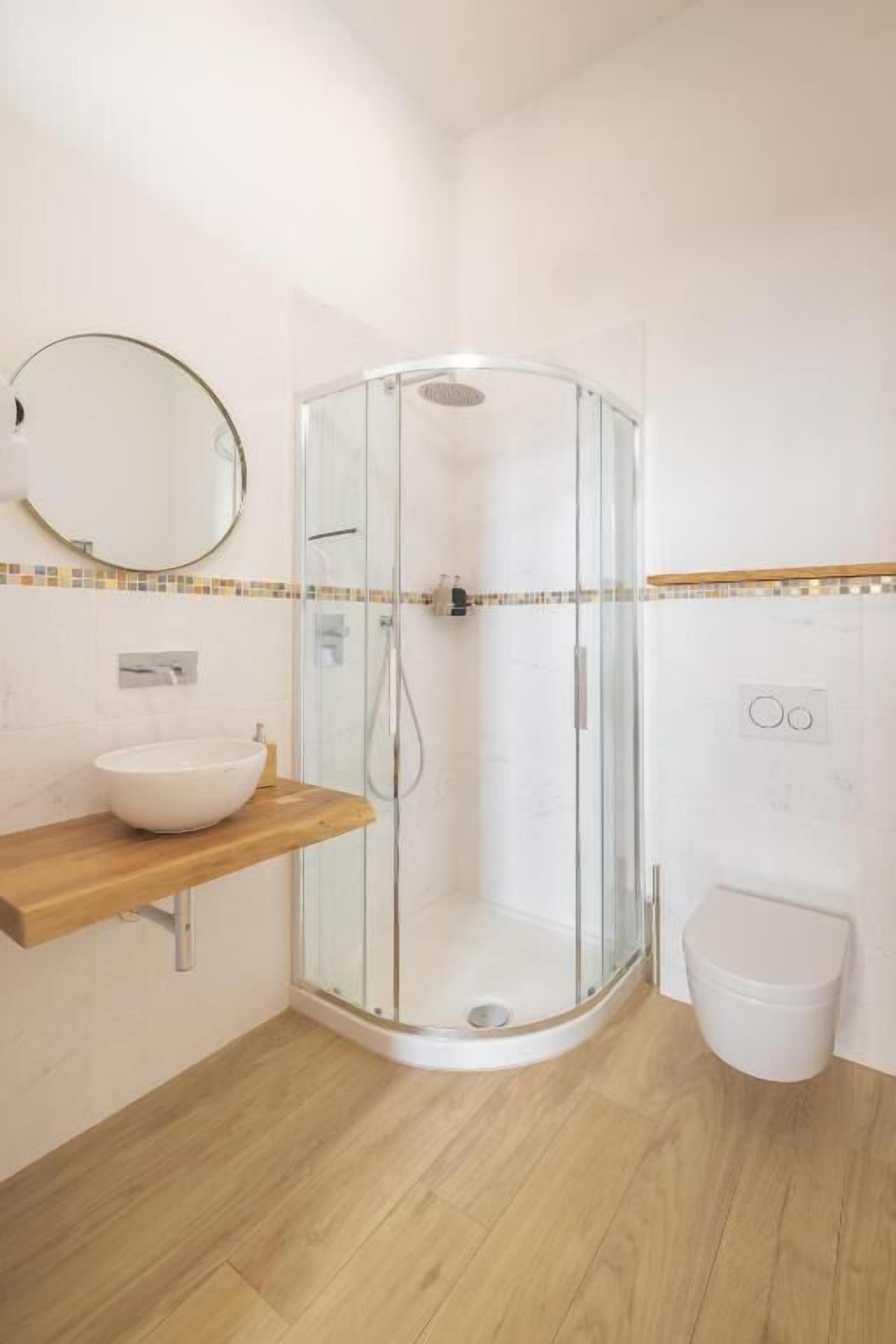 A bathroom with a glass shower enclosure, a wooden vanity with a sink, and a toilet.