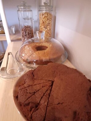 A wooden table with a bundt cake, a plate of brownies, and two glass jars with food items. - Casaldo's rooms (Florence)