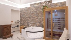 Ein moderner Wellnessraum mit Glastisch, Massagestuhl, Whirlpool und Holzschrank.