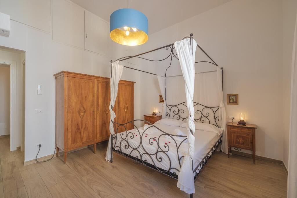 A four-poster bed with a canopy, a wooden wardrobe, a bedside table with a lamp, and a blue ceiling light.