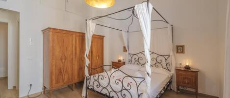 A four-poster bed with a canopy, a wooden wardrobe, a bedside table with a lamp, and a blue ceiling light.