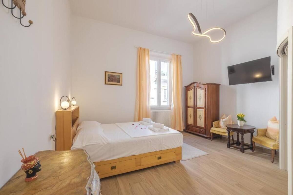 A bedroom with a bed, wooden dresser, and a TV mounted on the wall.