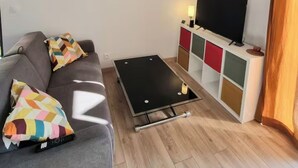 Un soggiorno moderno con un divano grigio, cuscini colorati, un tavolino da caffè nero, un televisore su un mobile multicolore e una lampada a sospensione geometrica.