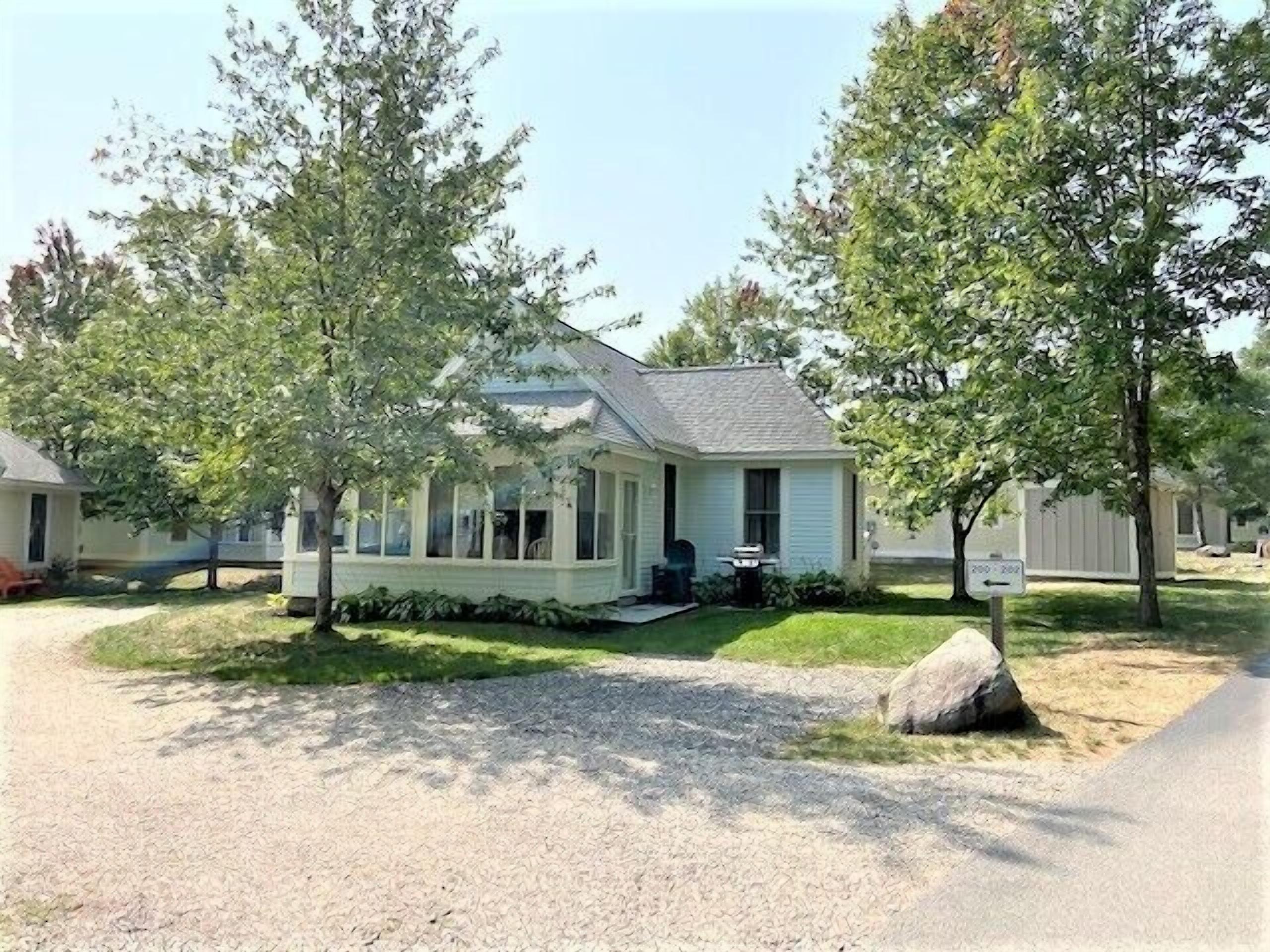 A single-story house with a front porch, a covered entryway, and a small front yard with a rock and a tree.