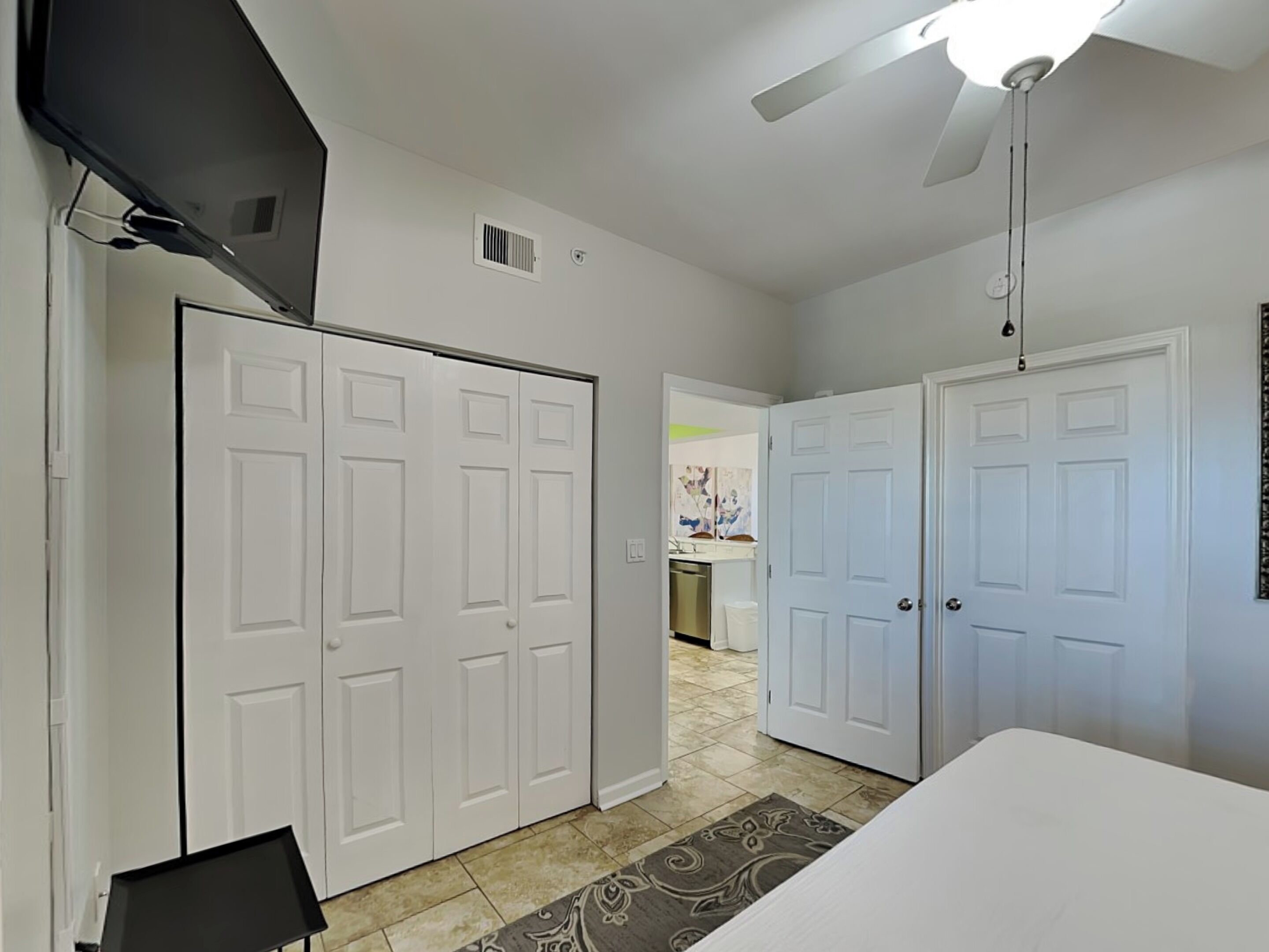 A bedroom with a bed, a ceiling fan, and a TV mounted on the wall.