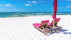 Ein Strand mit zwei Holzliegen und einem roten Sonnenschirm.