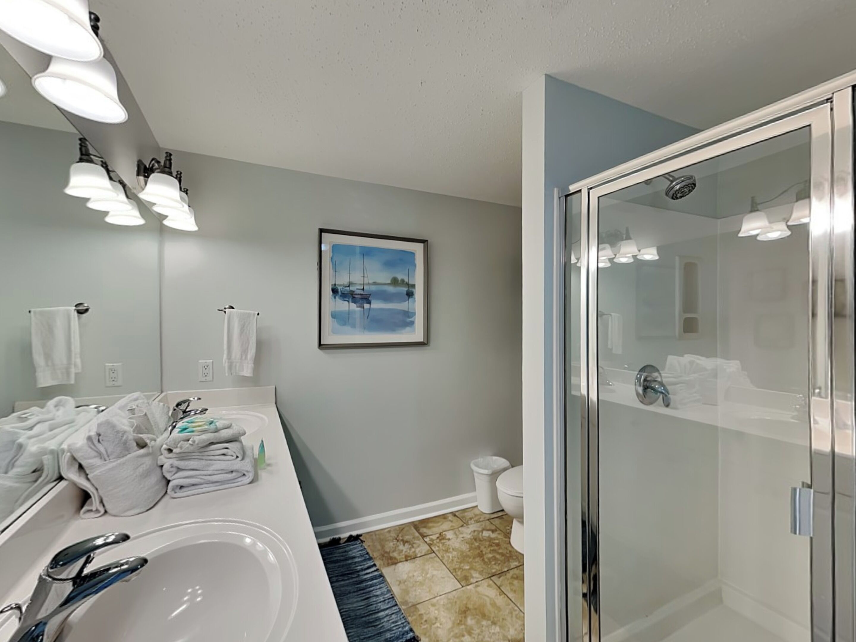 A bathroom with a large mirror, a sink, a glass shower enclosure, and a framed painting on the wall.