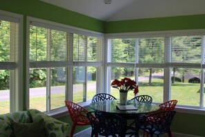 A room with a glass table and chairs, a vase with flowers, and large windows with blinds.