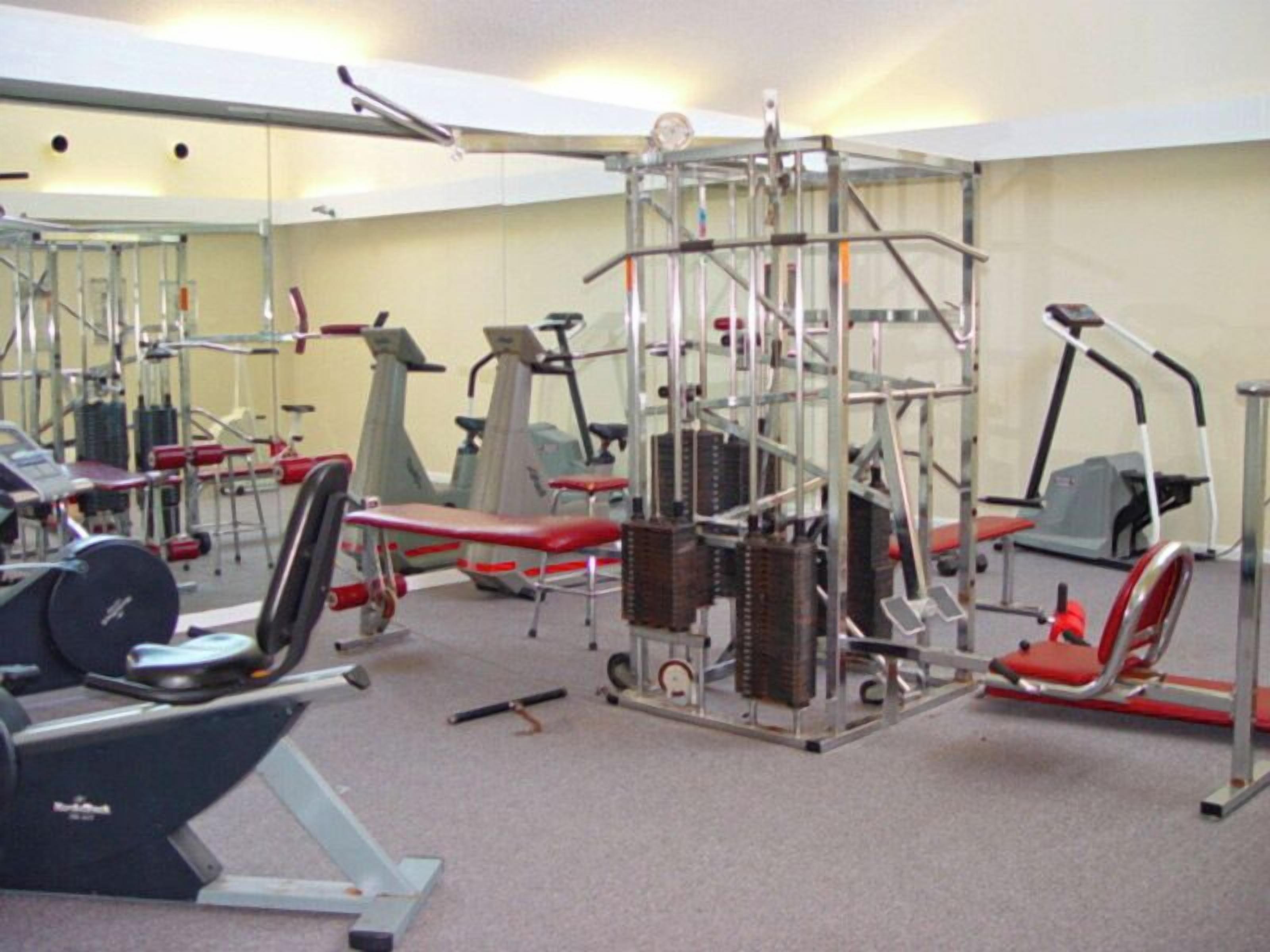 Une salle de sport équipée de divers appareils d’exercice, notamment des tapis de course, des appareils de musculation et des poids libres.