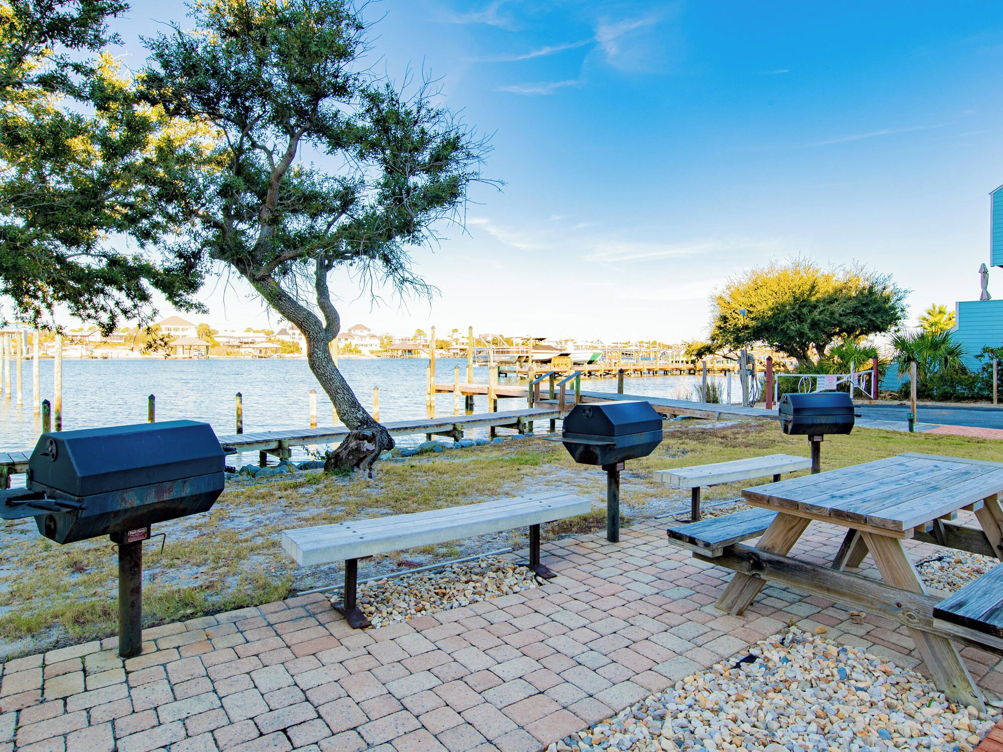 An outdoor patio with picnic tables and barbecue grills by a waterfront.