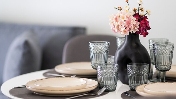 A dining table set with plates, cutlery, and glasses, accompanied by a vase of flowers. - Modern Rooms Exarchia Room 2 (Athina)
