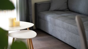 A modern living room with a grey sofa, a small white table with candles, and a green plant in the foreground. - Modern Rooms Exarchia Room 2 (Athina)
