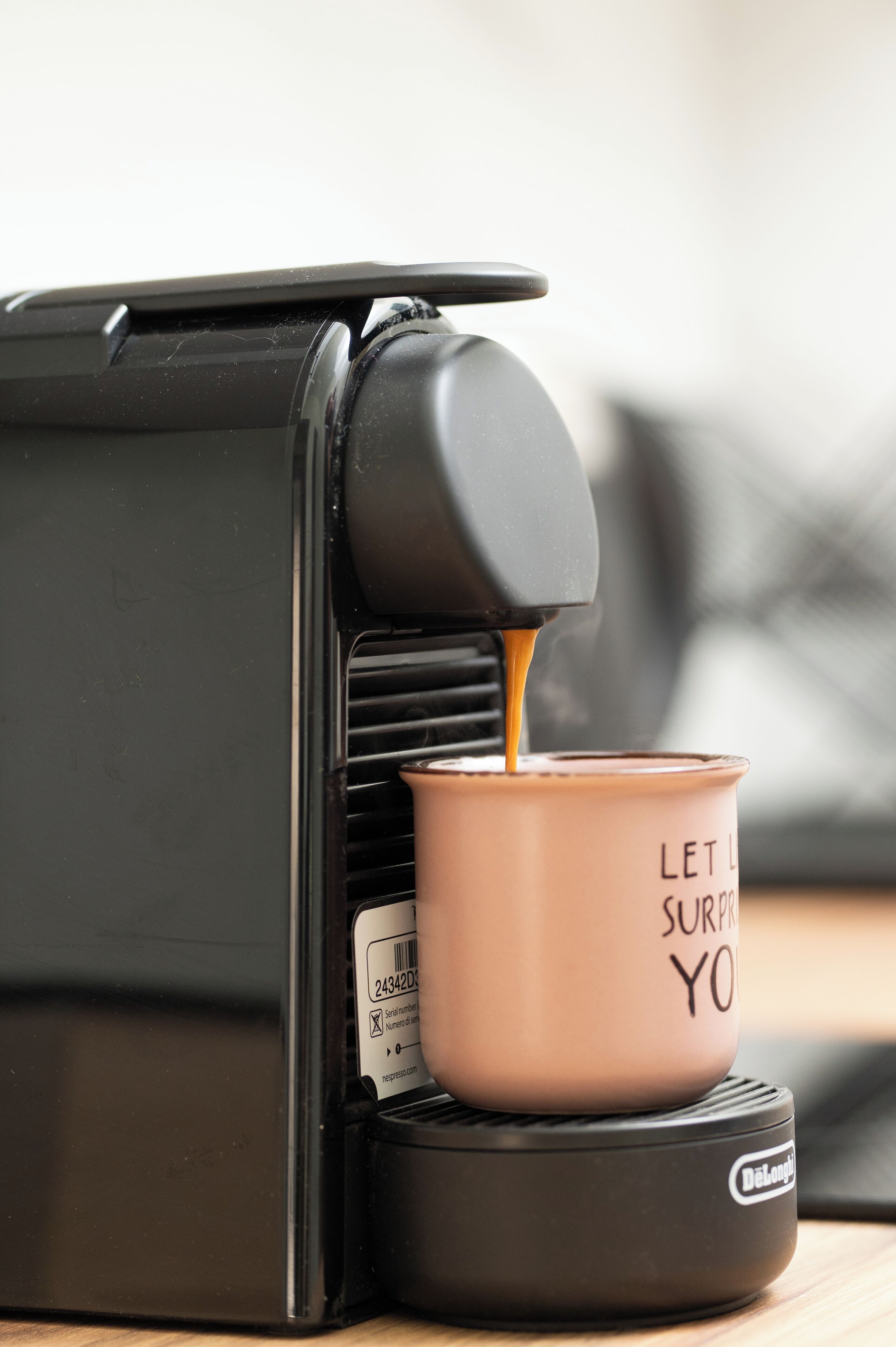 A coffee machine dispensing coffee into a mug with the text "LET IT SURPRISE YOU".