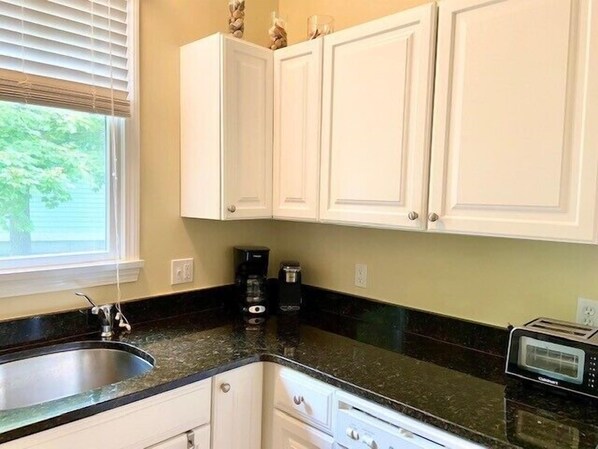 A kitchen with white cabinets, a black countertop, a sink, a coffee maker, and a toaster.