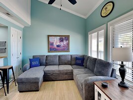 A cozy living room with a gray sectional sofa, a wooden coffee table, and a framed painting of a sailboat on the wall.