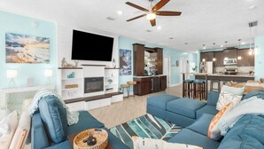 A modern living room with a fireplace, a flat-screen TV, and a dining area with bar stools. - Orange Crush by Resort Collection (Panama City Beach)