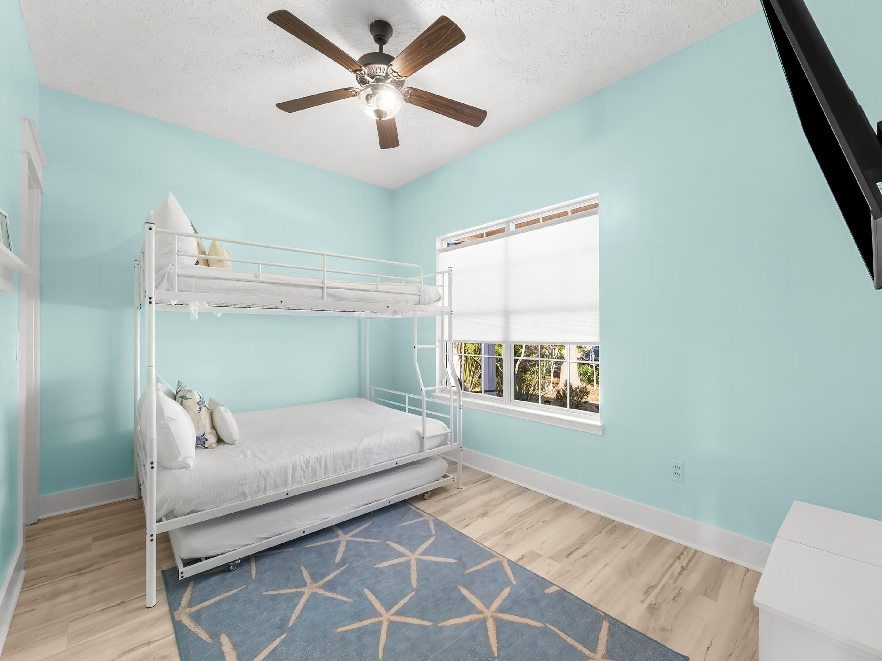 A bunk bed room with a ceiling fan, a window with blinds, and a star-patterned rug.