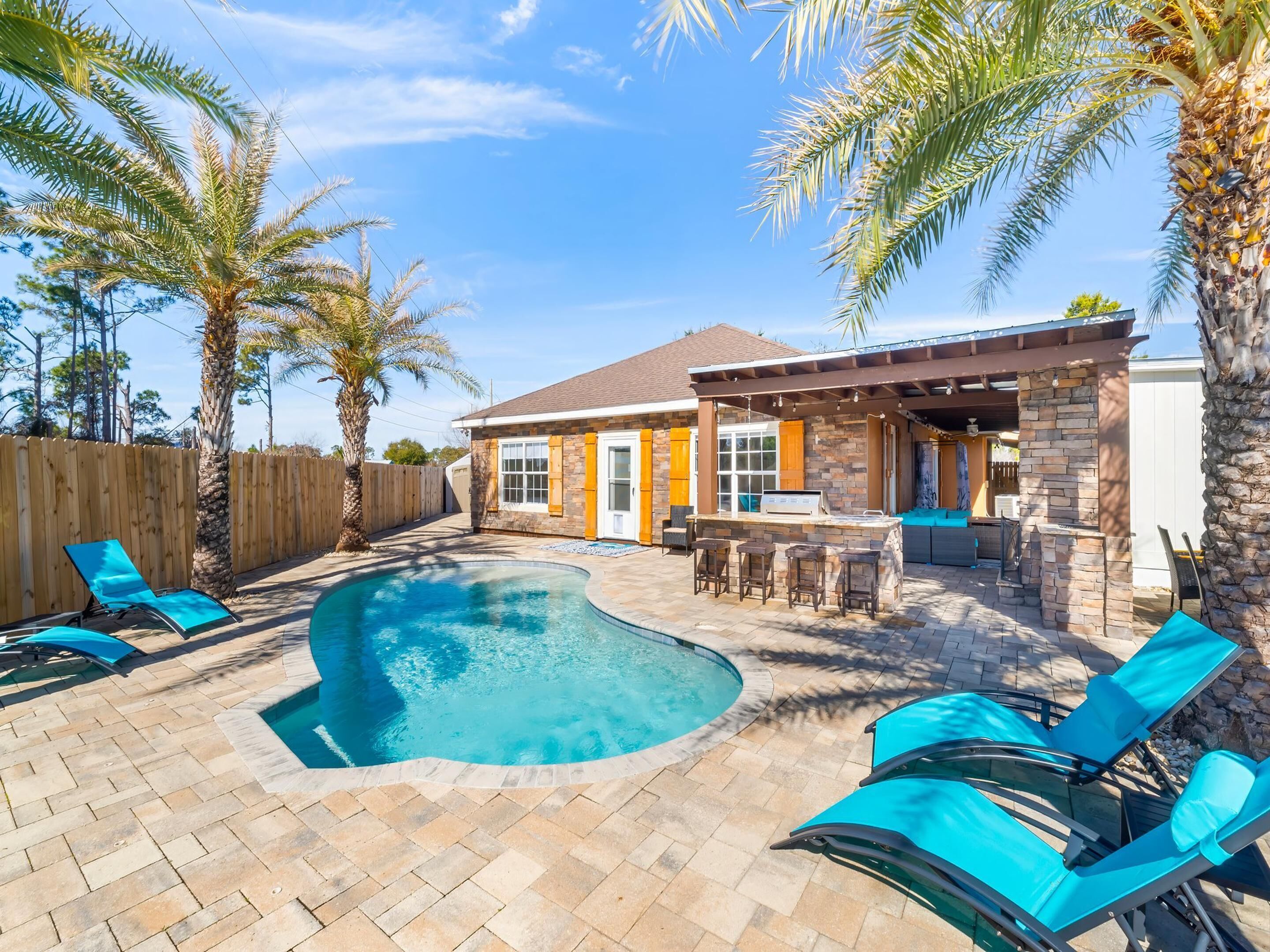 A backyard with a swimming pool, lounge chairs, and a barbecue area.