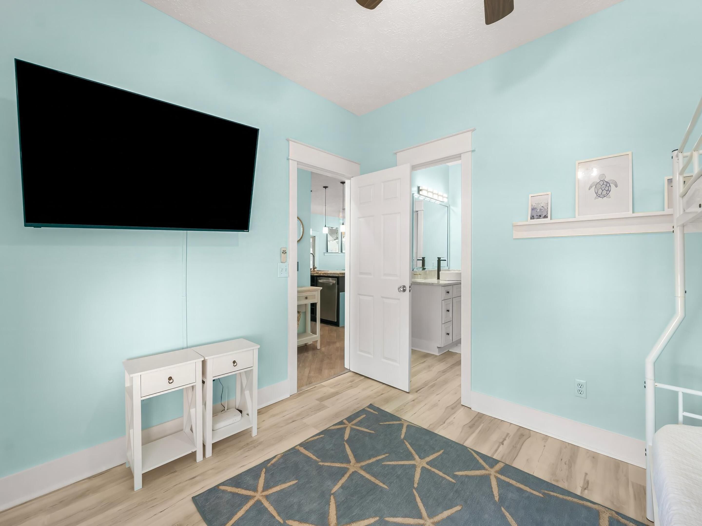 Une pièce dotée d’un téléviseur à écran plat, d’une console blanche, d’un tapis à motifs et d’une porte donnant accès à une salle de bain.