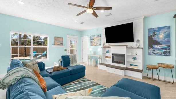 Un salón espacioso con un sofá azul, una chimenea, un televisor de pantalla plana y un ventilador de techo.