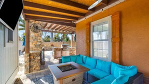 A covered outdoor patio with a stone fireplace, a grill, and a blue sofa. - Orange Crush by Resort Collection (Panama City Beach)